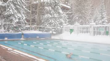 Piscina com divisórias de pista, rodeada por árvores cobertas de neve e um edifício com placa de aviso.