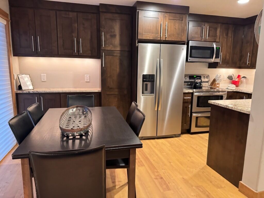 Una cocina moderna con armarios de madera oscura, electrodomésticos de acero inoxidable y una zona de comedor con mesa y sillas.
