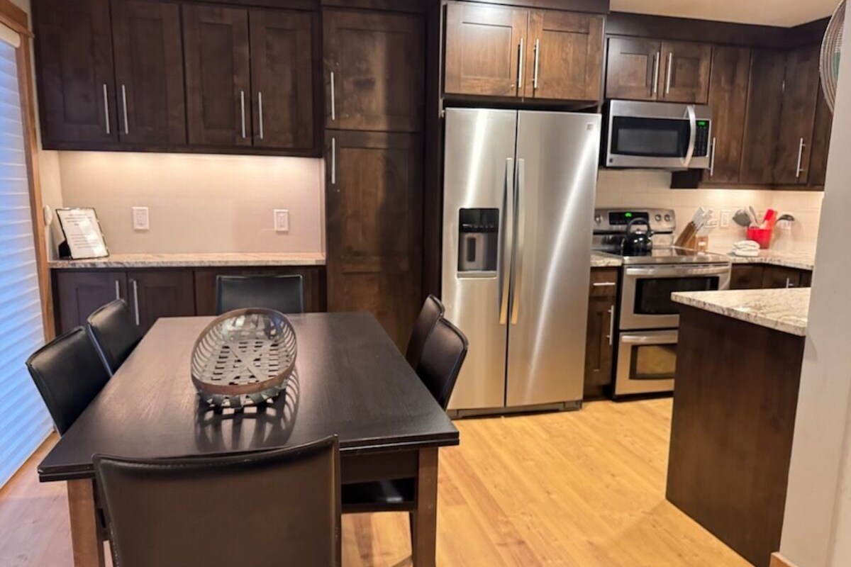 Una cocina moderna con armarios de madera oscura, electrodomésticos de acero inoxidable y una zona de comedor con mesa y sillas.