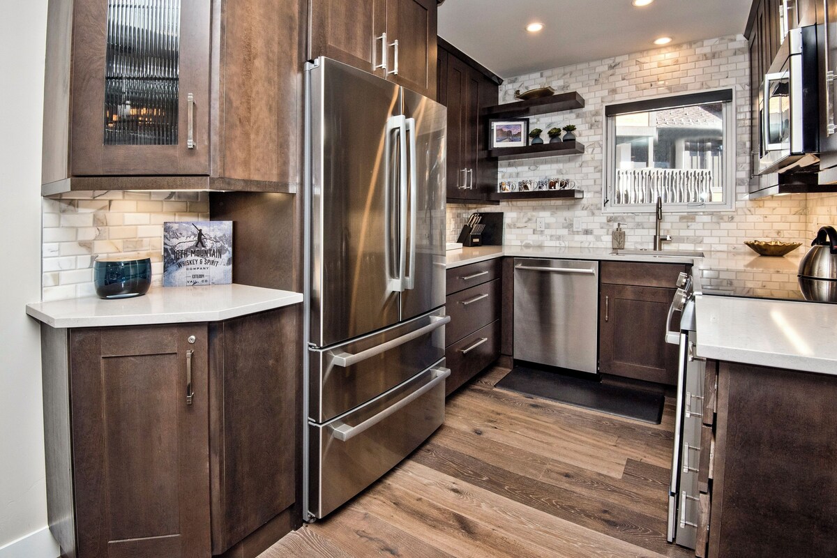 Una cocina moderna con armarios de madera oscura, electrodomésticos de acero inoxidable y un salpicadero de azulejos blancos.