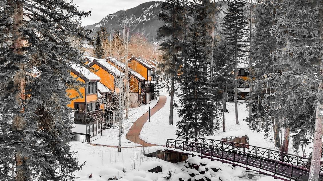 A snow-covered landscape with a wooden bridge and buildings with orange facades.