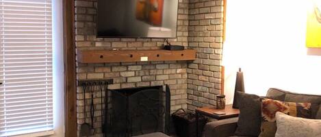 Ein Wohnzimmer mit Kamin aus Ziegelsteinen, einem Wand-Fernseher, einer Couch und einem Couchtisch mit Dekoration.