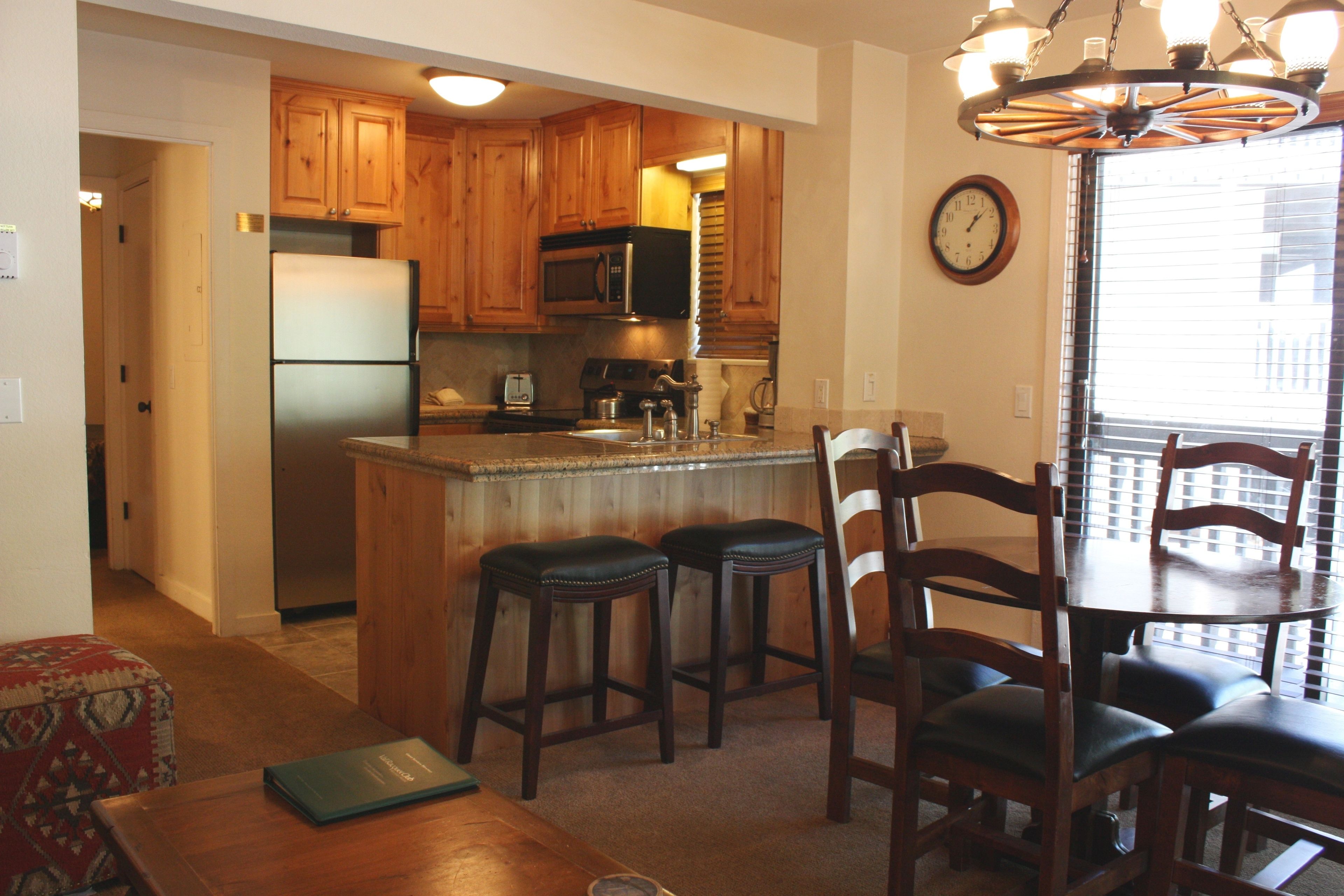 A kitchen with wooden cabinets, a refrigerator, a microwave, and a dining area with a table and chairs.