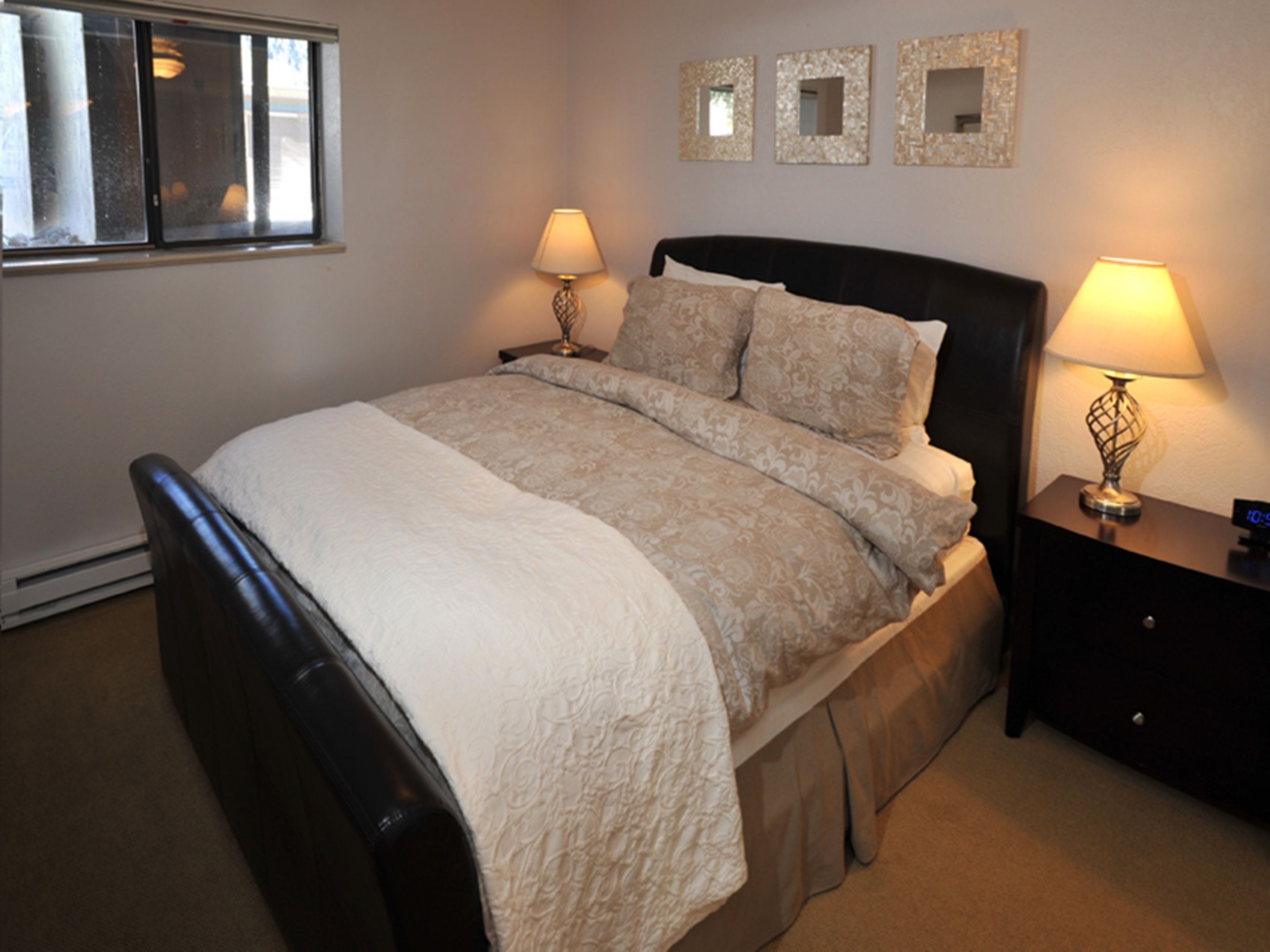 A neatly arranged bedroom with a bed, two bedside tables with lamps, and three wall-mounted mirrors.