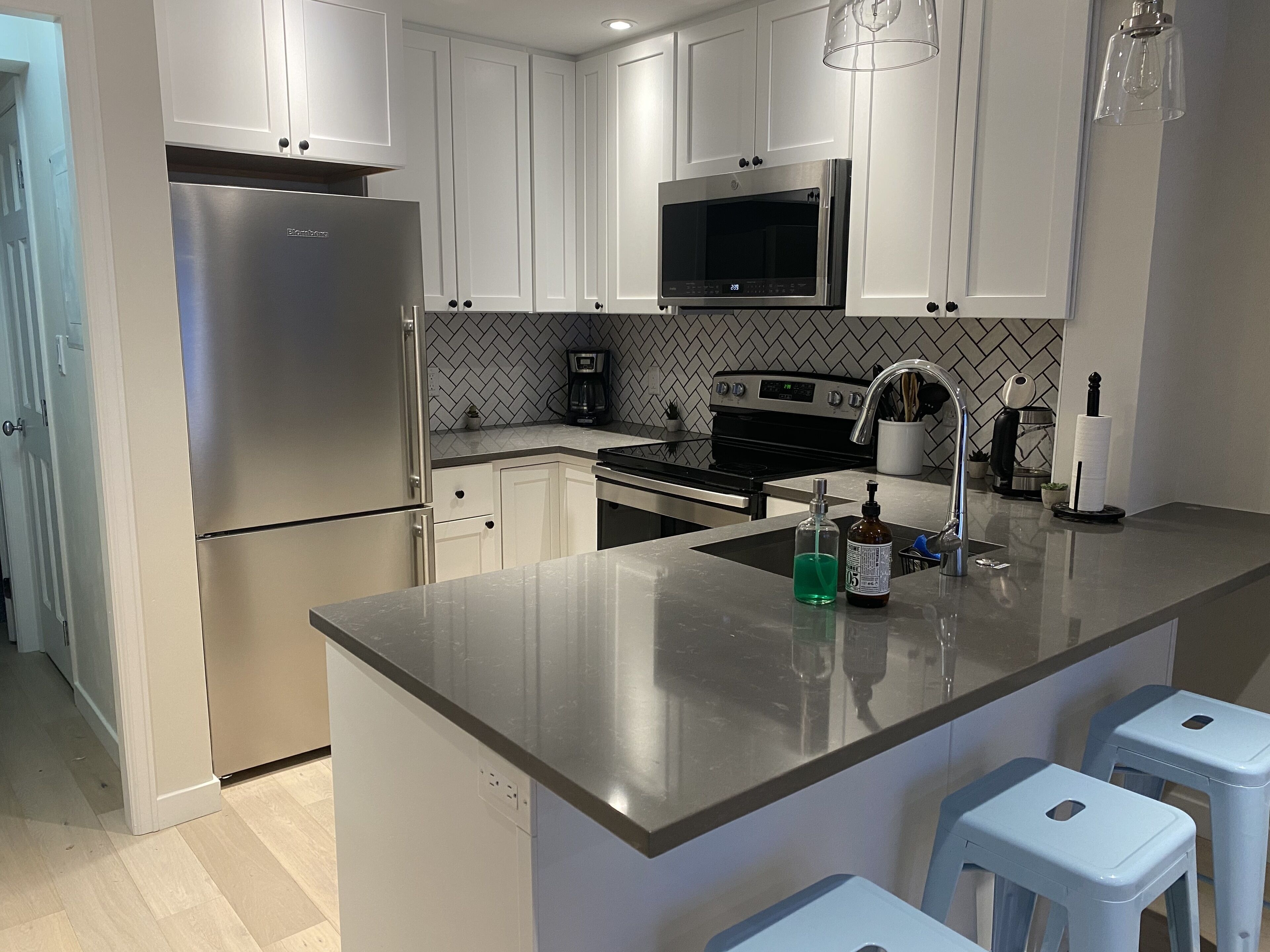 A modern kitchen with white cabinets, stainless steel appliances, a central island, and bar stools.
