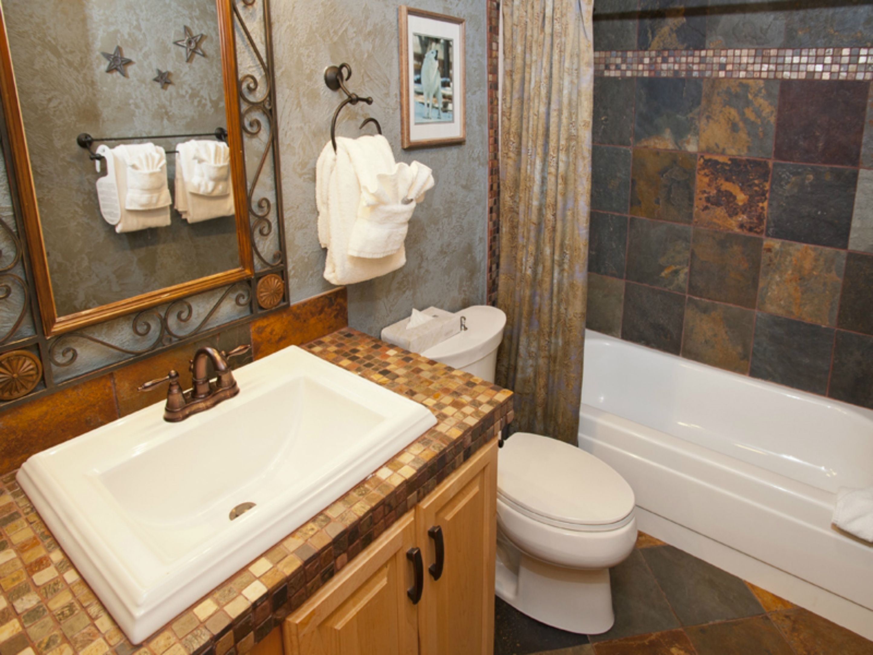 A bathroom with a large white sink, a toilet, and a bathtub. There are towels hanging on a rack and a framed picture on the wall.