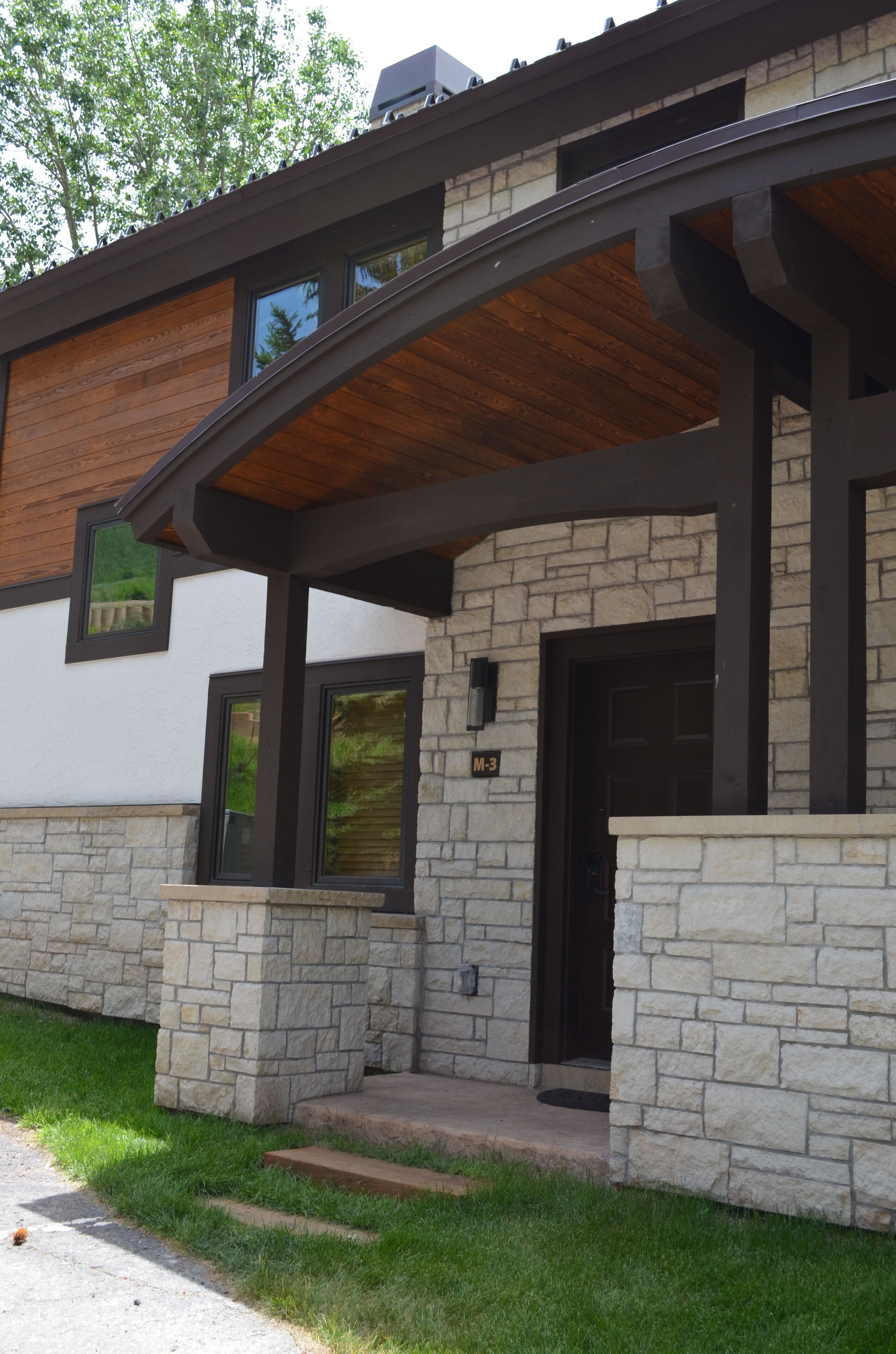 A modern house with a stone facade, a wooden deck, and a black door.