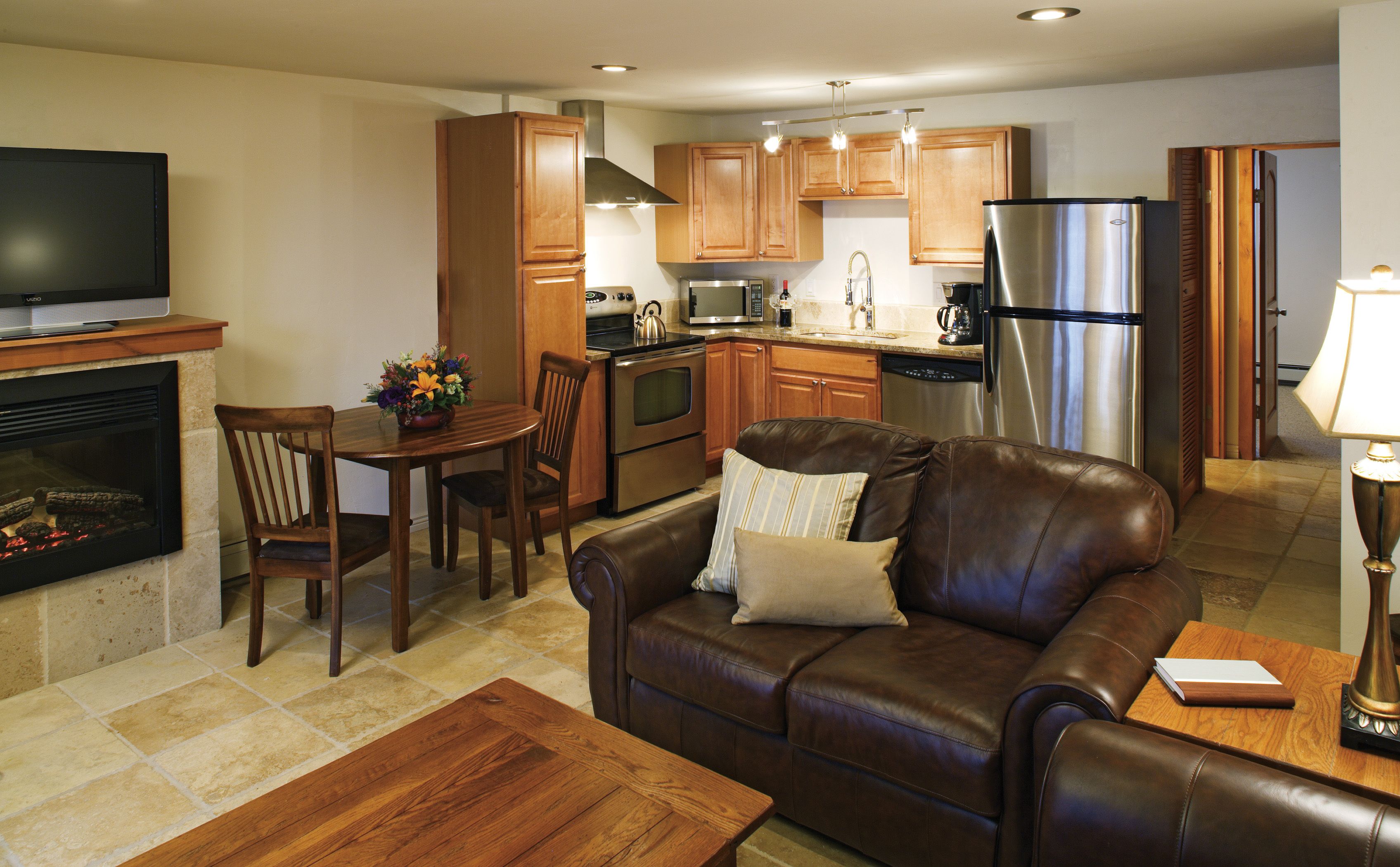 A modern kitchen with wooden cabinets, stainless steel appliances, and a dining area with a leather sofa and a fireplace.