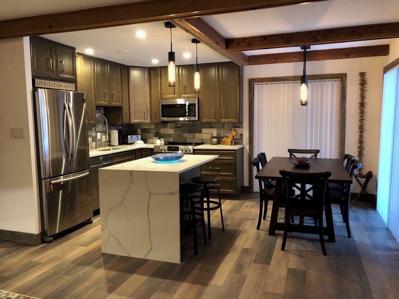 A modern kitchen with stainless steel appliances, a marble island, and a dining area with wooden furniture.