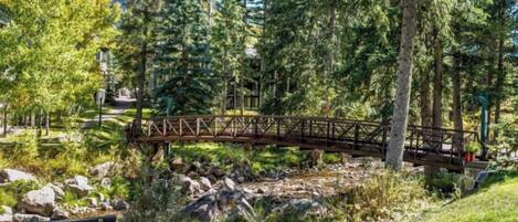A wooden bridge over a rocky stream in a forested area with a bench and trees.