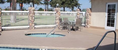 A swimming pool with a stone wall and a white fence, surrounded by trees and a building.
