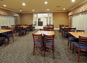 A hotel dining room with multiple tables and chairs, carpeted flooring, and a view of the hotel lobby. - Holiday Inn Express Hotel & Suites Corning by IHG (Corning)