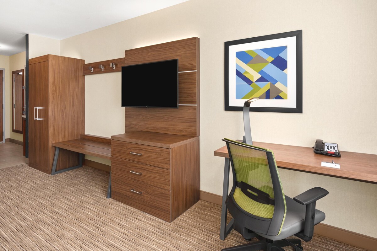 A modern office space with a wooden desk, a chair, a flat-screen TV, and a framed abstract art piece on the wall.