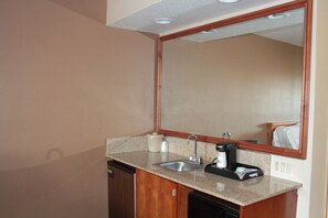 A small kitchenette with a sink, a coffee maker, and a mirror above the counter. - Holiday Inn Express Hotel & Suites Corning by IHG (Corning)