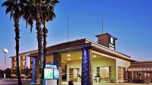 A Holiday Inn Express building with a clear sky, palm trees, and a well-lit entrance.