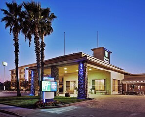 A Holiday Inn Express building with a clear sky, palm trees, and a well-lit entrance. - Holiday Inn Express Hotel & Suites Corning by IHG (Corning)