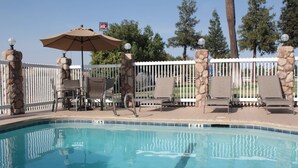 A swimming pool with lounge chairs and an umbrella, surrounded by a white fence and stone pillars.