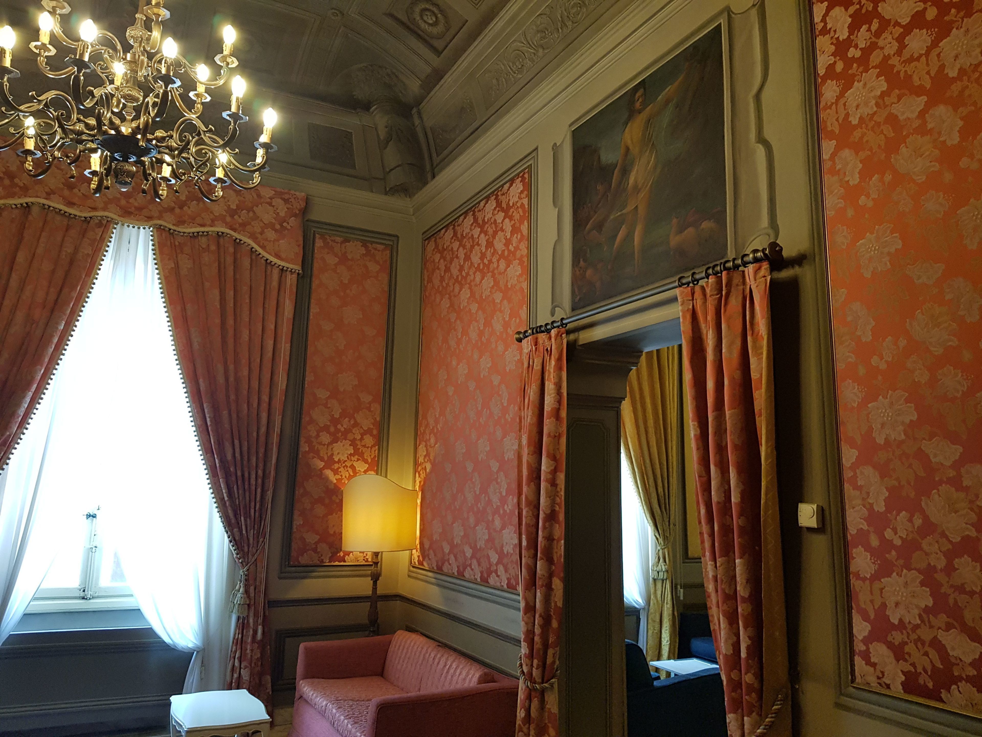 A room with a chandelier, floral wallpaper, a sofa, and a painting on the wall.