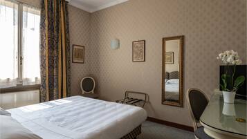 A hotel room with a large bed, a small table, a chair, a mirror, and a potted plant.