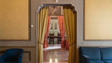 Un pasillo con un sofá azul, un comedor con candelabro y una puerta con cortinas rojas.