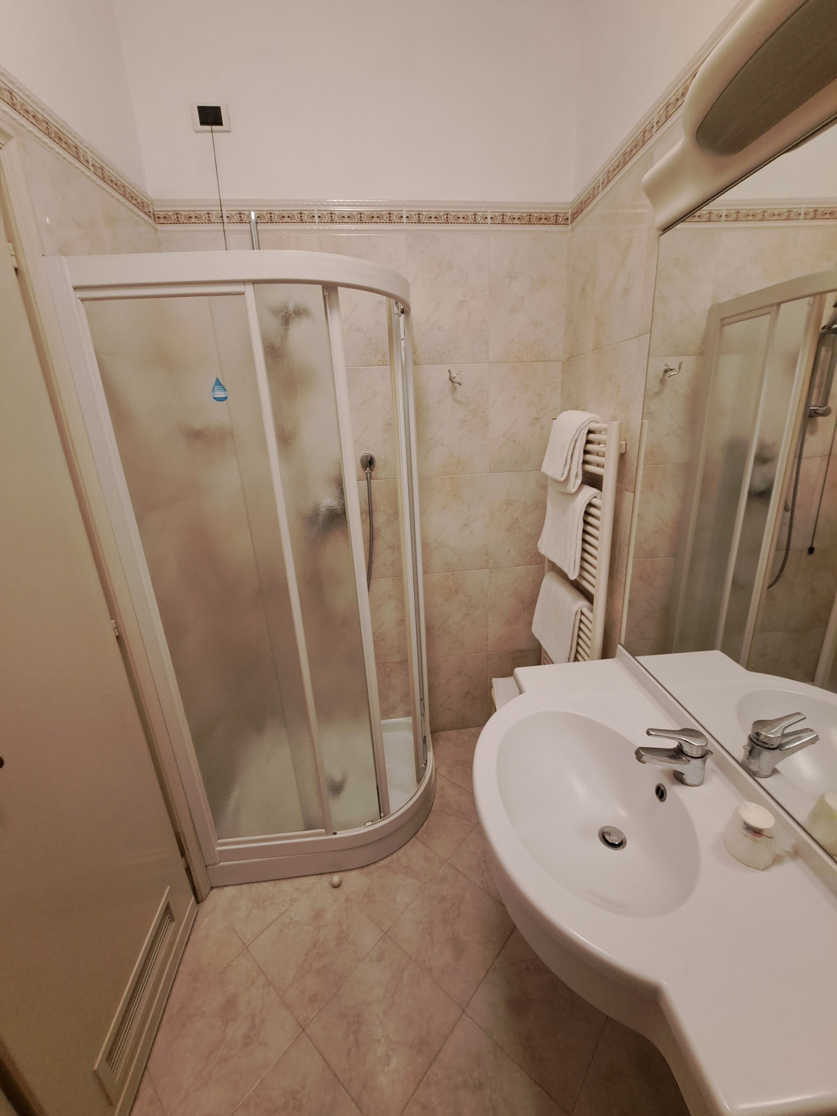 Een badkamer met een glazen douchecabine, een wastafel met spiegel en een handdoekrek.