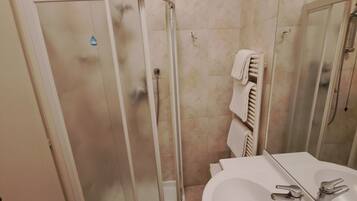Een badkamer met een glazen douchecabine, een wastafel met spiegel en een handdoekrek.