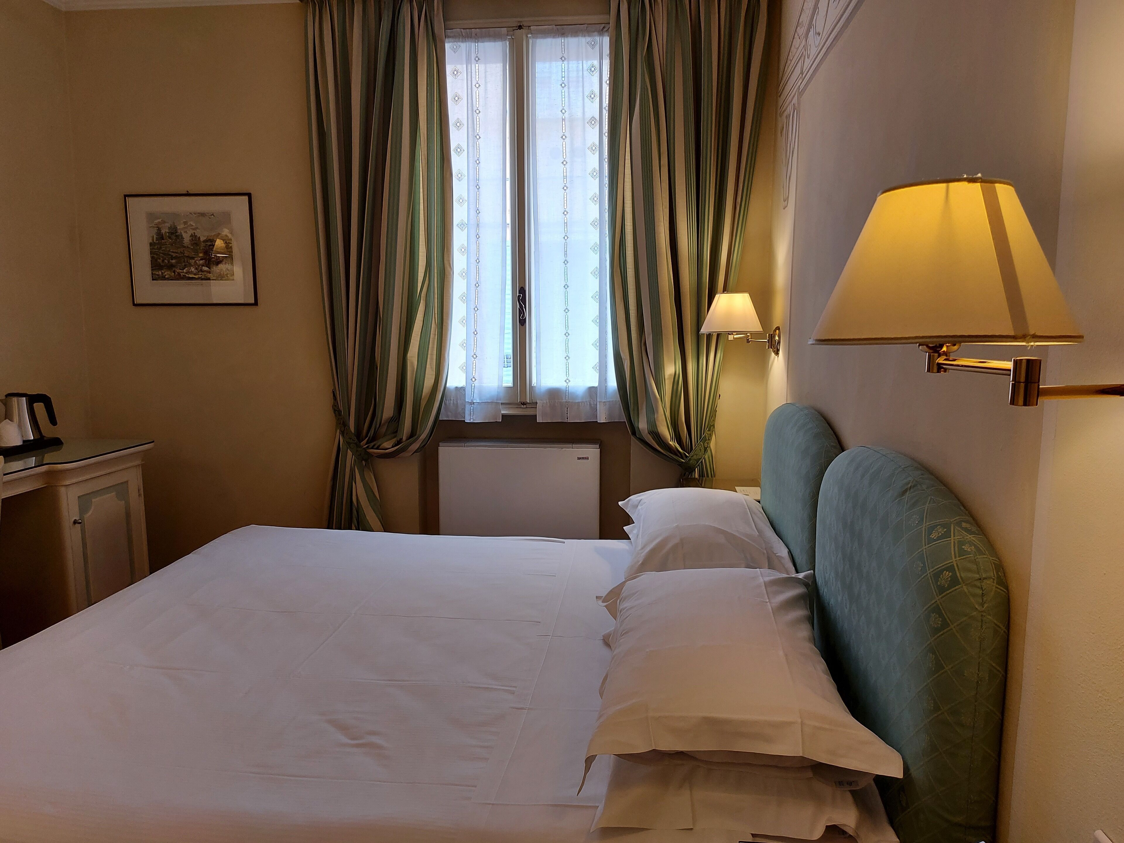 Une chambre d’hôtel avec un lit, une table de chevet, une lampe et une fenêtre avec des rideaux.