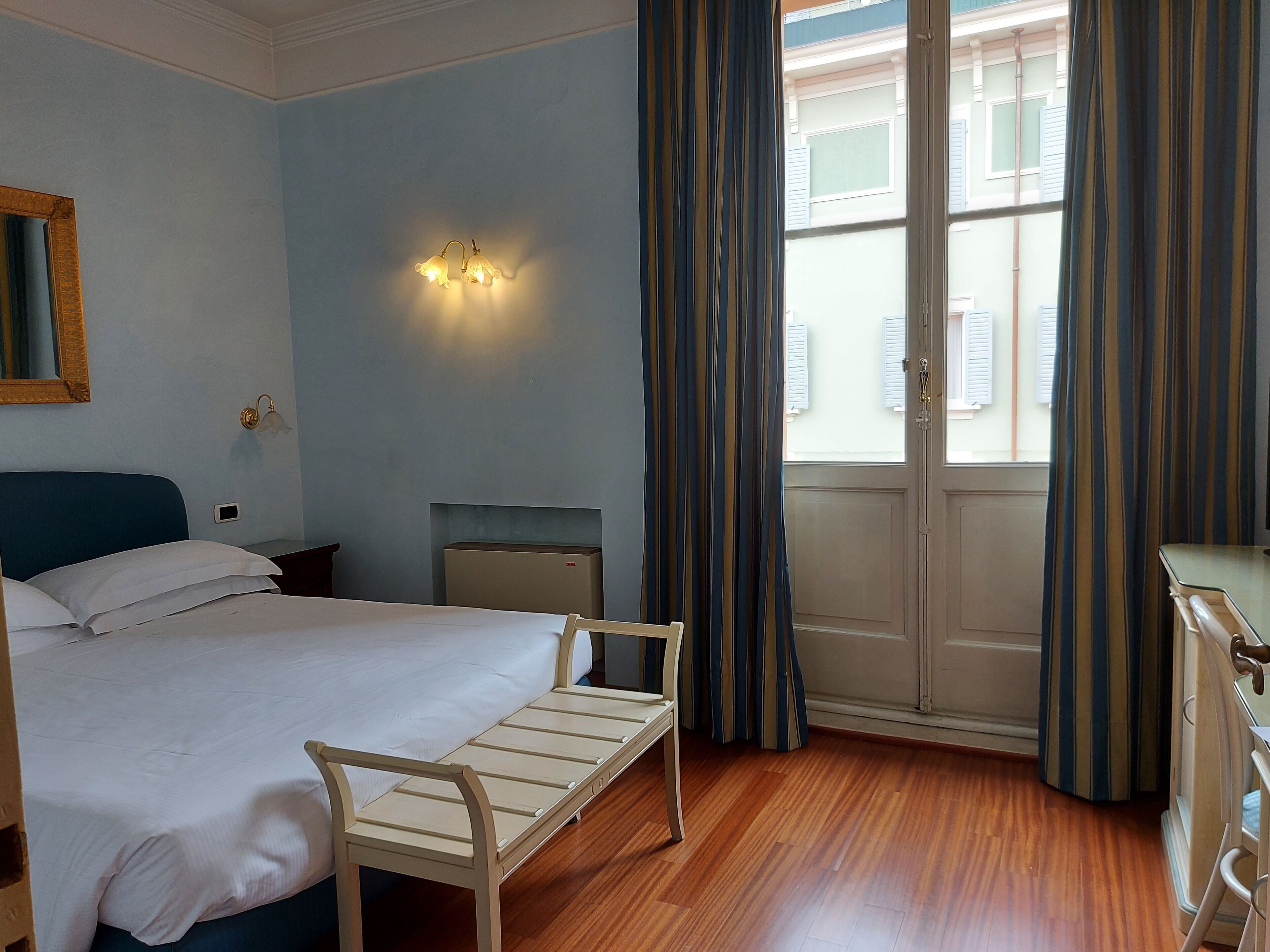 Habitación de hotel con cama, mesita de noche, lámpara y vistas a través de una puerta.
