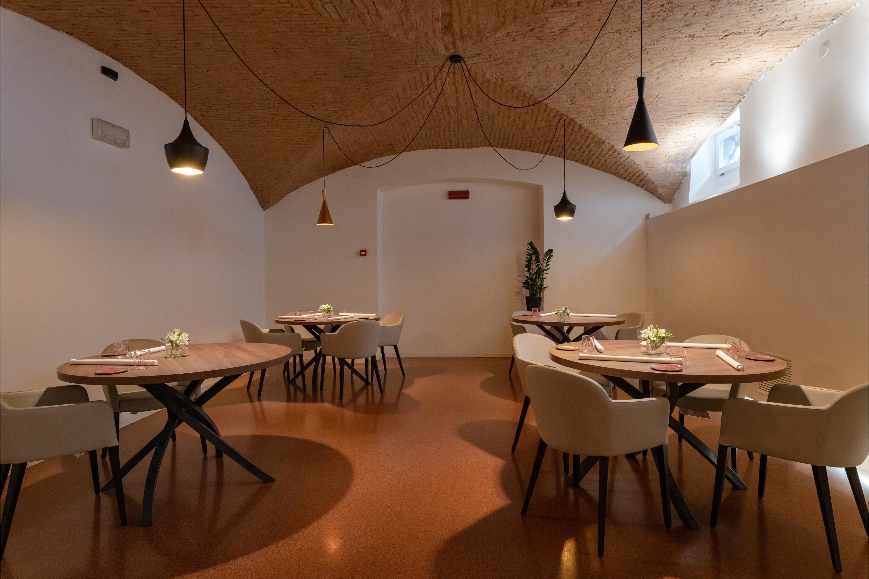A modern dining area with round tables and chairs, wooden ceiling, and pendant lighting.
