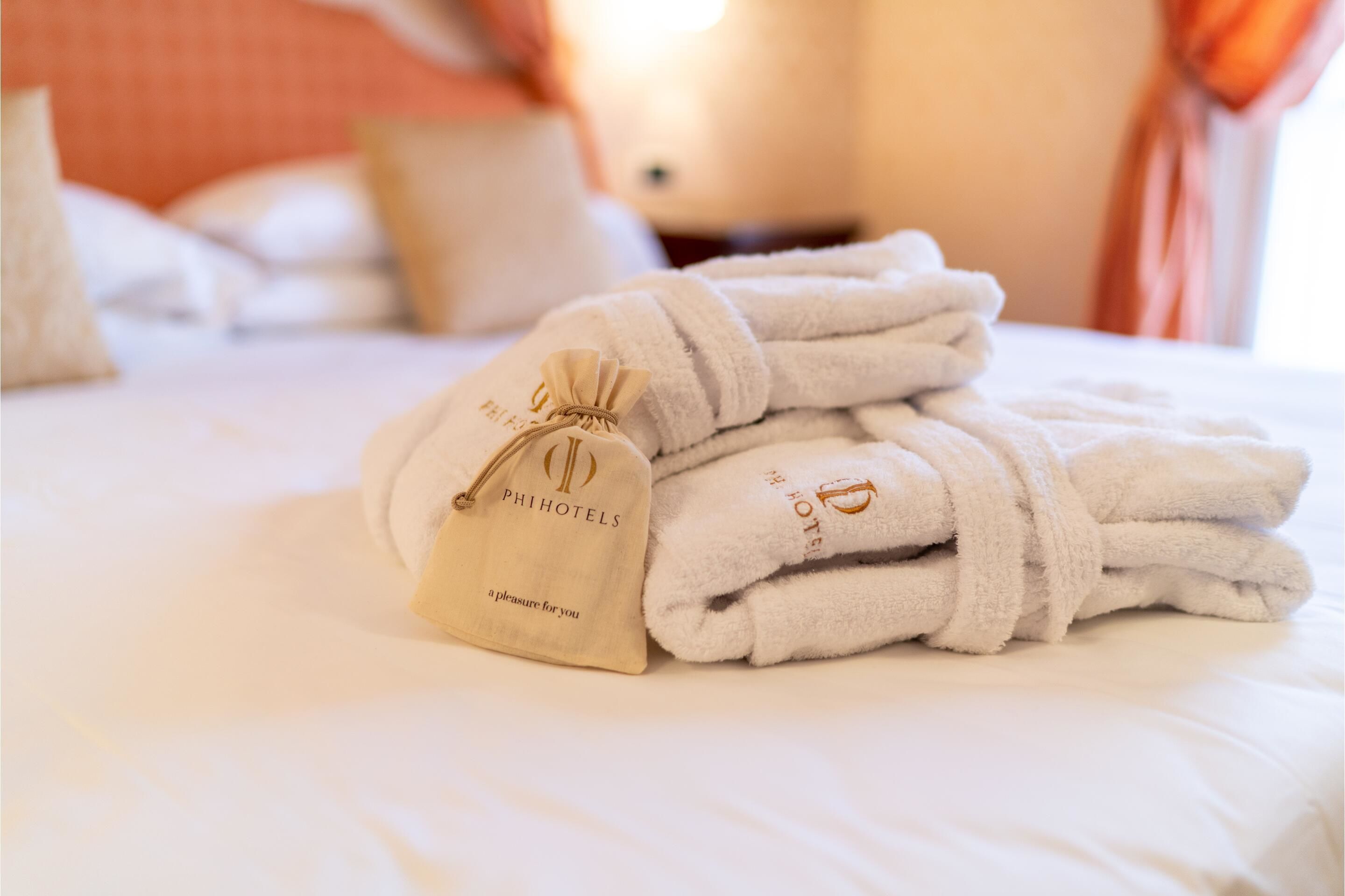 Un lit parfaitement fait, avec des serviettes blanches pliées et un sac à serviettes de la marque PHIHOTELS.