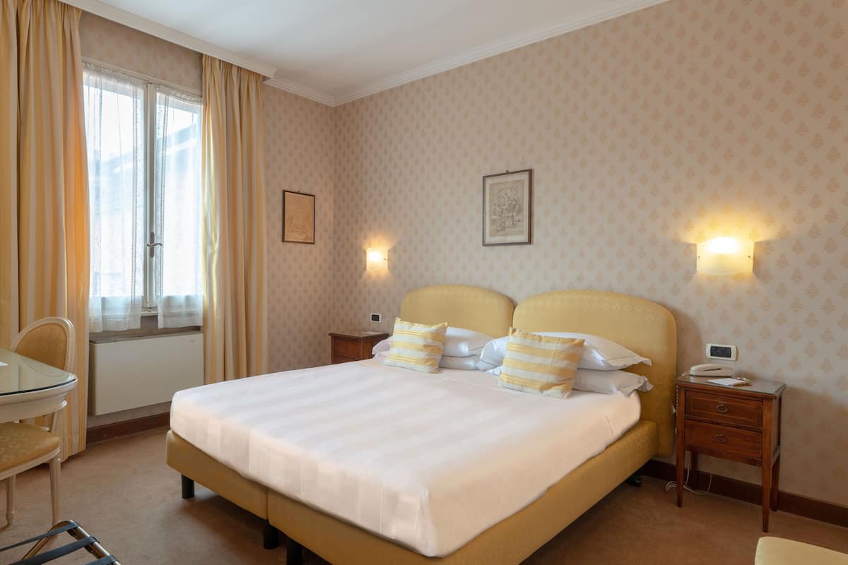 Una habitación de hotel con una cama grande, mesitas de noche, un escritorio y una silla.