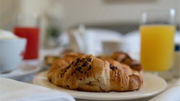 Une table mise pour le petit-déjeuner avec des croissants sur une assiette, un verre de jus d’orange et une tasse rouge.