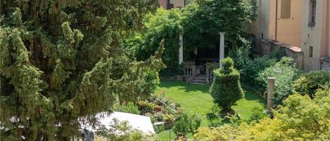 A courtyard with a lawn, trees, and a building with a tiled roof.