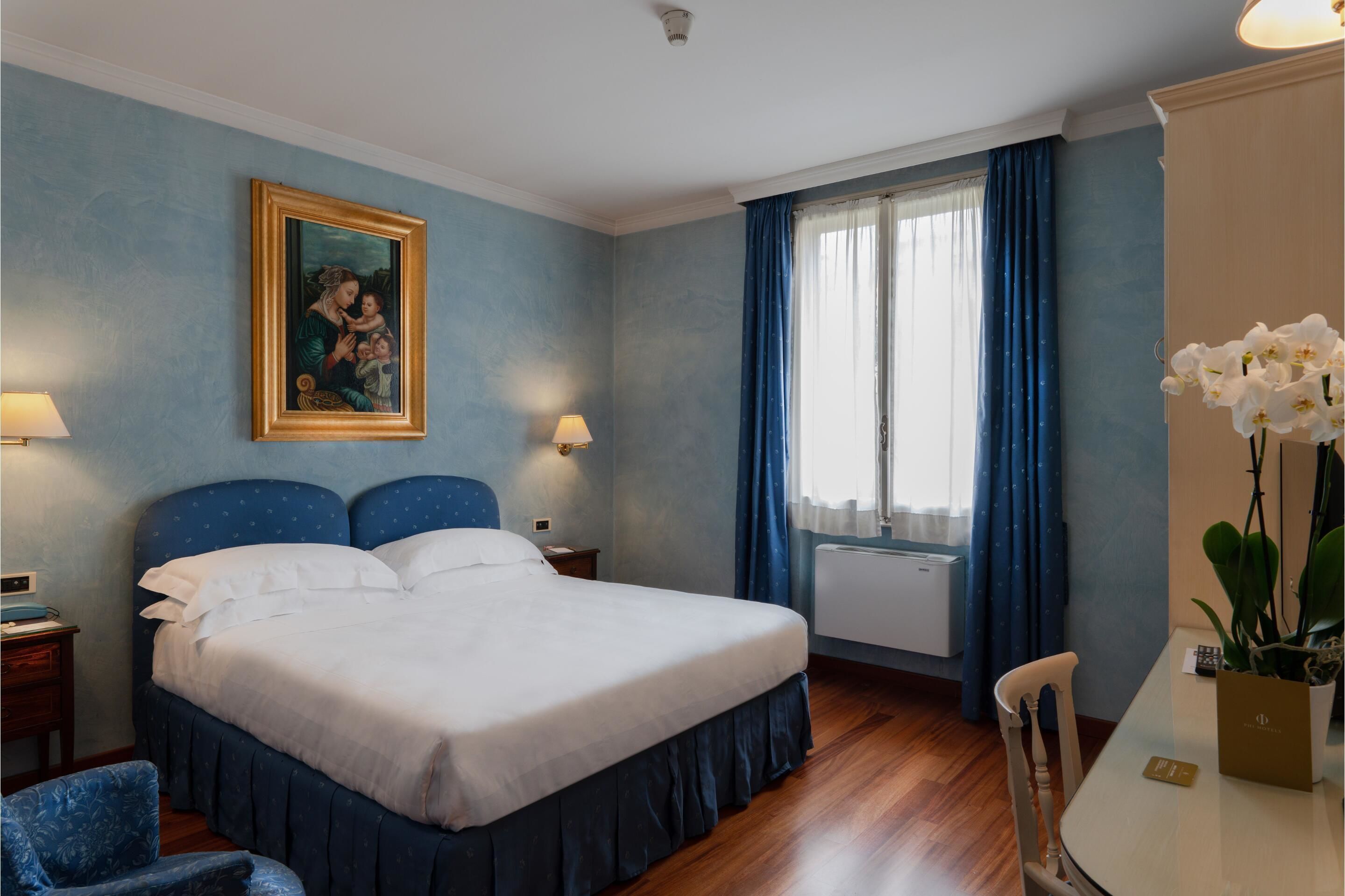 Une chambre d’hôtel avec un grand lit, deux tables de chevet, un bureau avec une chaise et une fenêtre avec des rideaux.