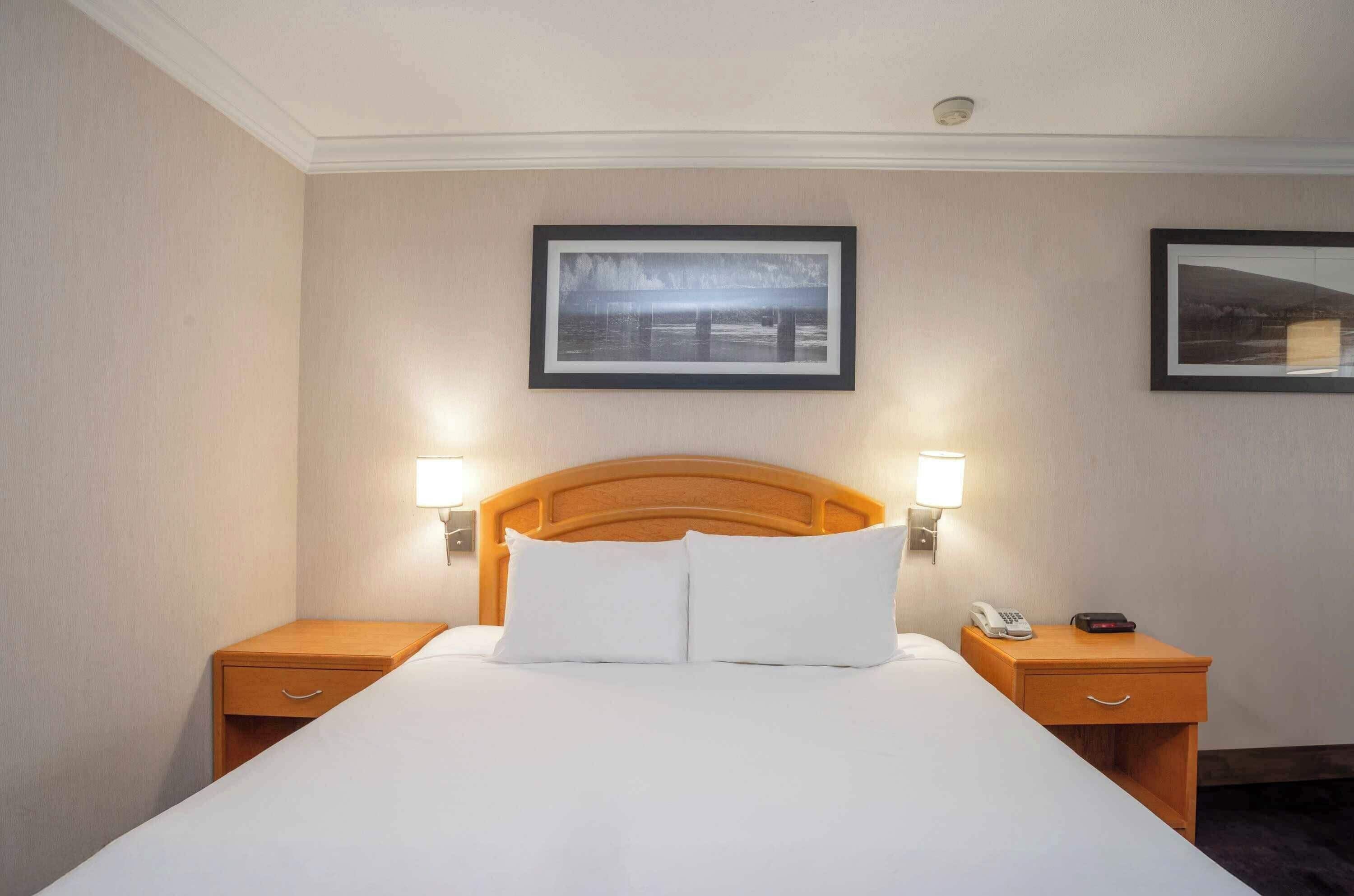 A hotel room with a large bed, two bedside tables, a wooden headboard, and two framed pictures on the walls.