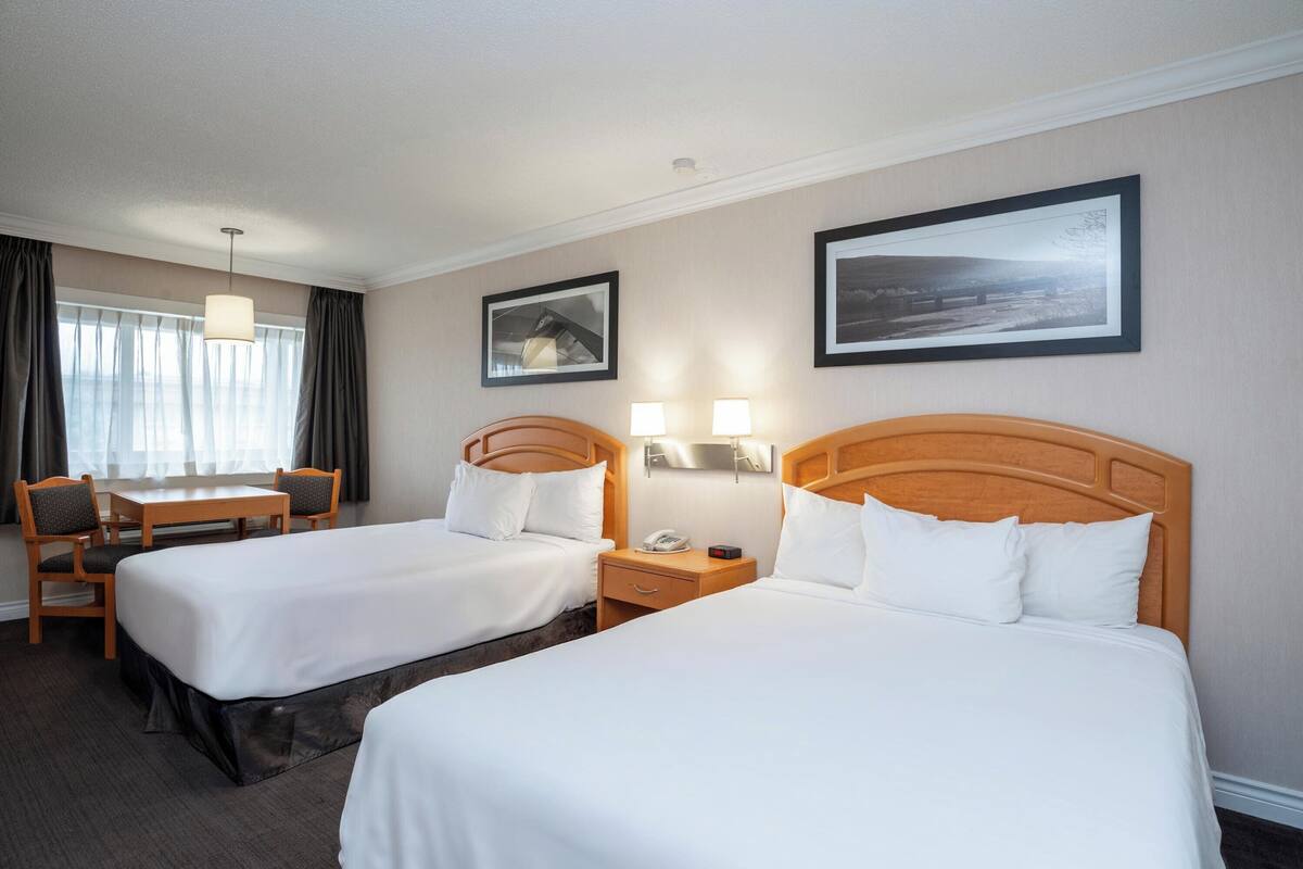 A hotel room with two beds, a desk, and a chair.