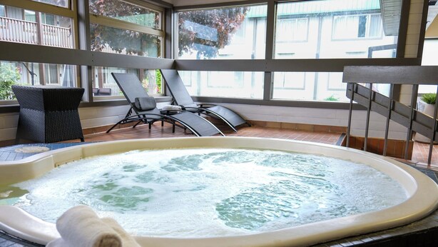 A hot tub with a view of the outside, surrounded by lounge chairs and a tiled floor.