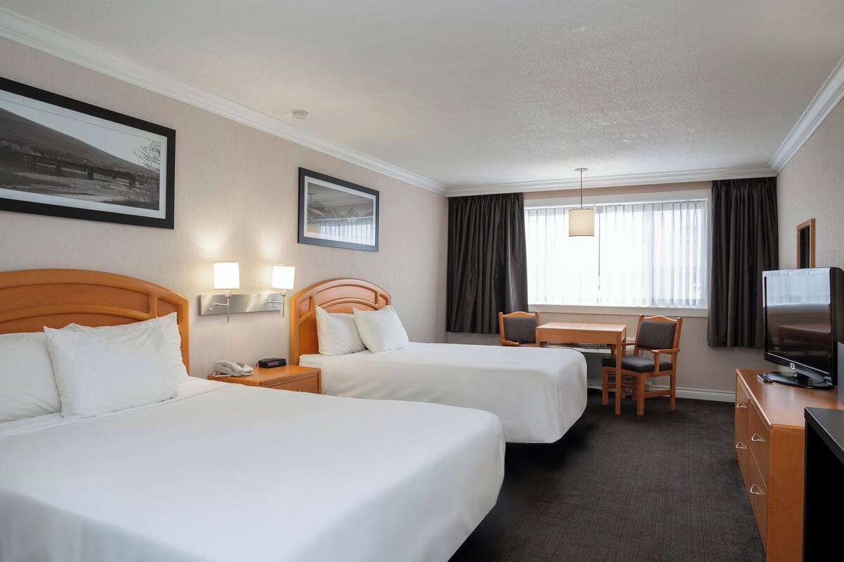 A hotel room with two beds, a desk with a chair, a television, and a window with curtains.