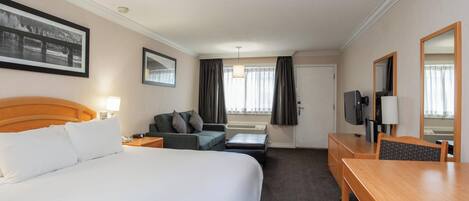 A hotel room with a large bed, a desk, a chair, a sofa, a television, and a window with curtains.