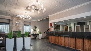 A lobby with a reception desk, a staircase, and a seating area with potted plants.