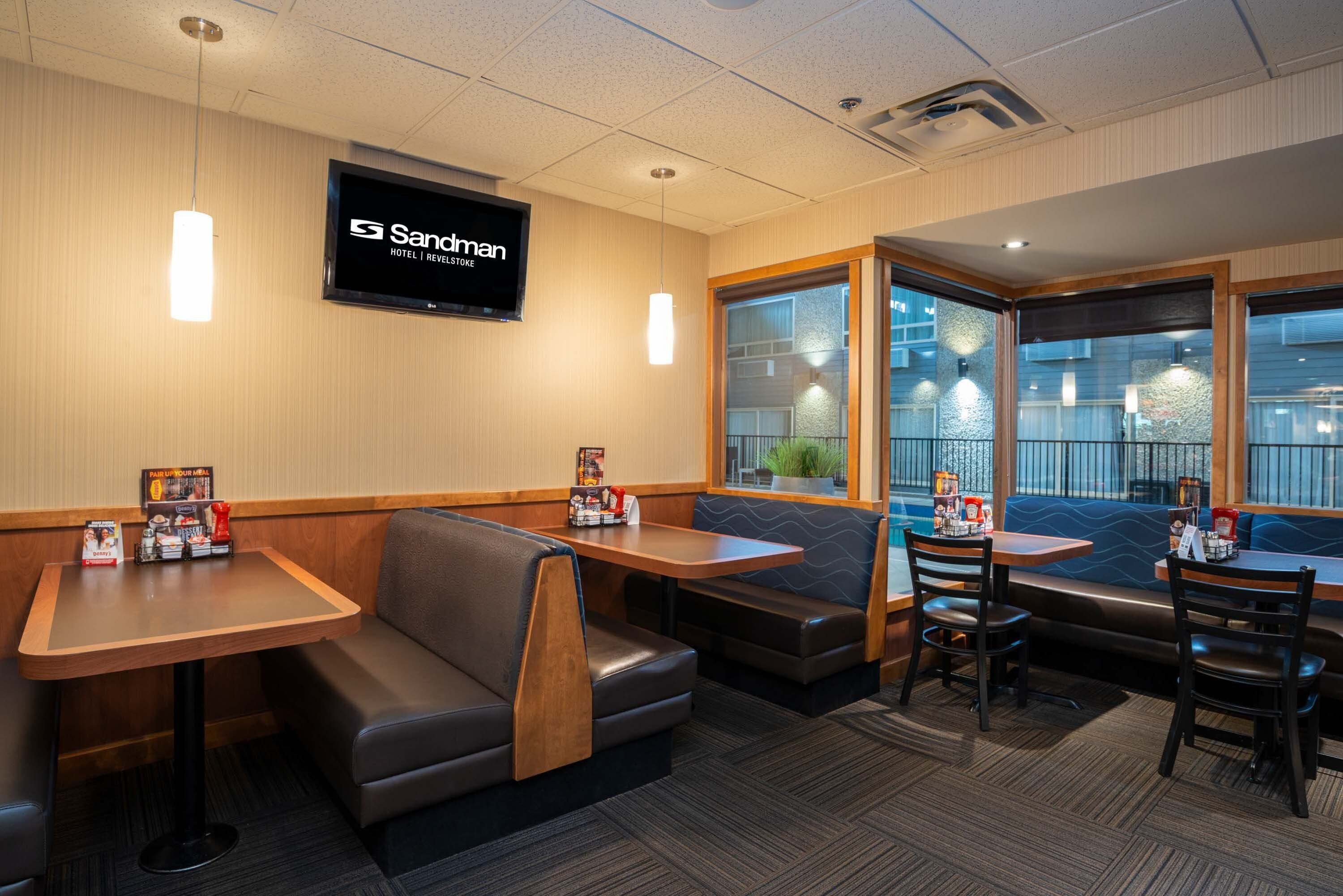 Un restaurant avec des banquettes et des tables, un téléviseur fixé au mur et une vue sur l’extérieur grâce à de grandes fenêtres.