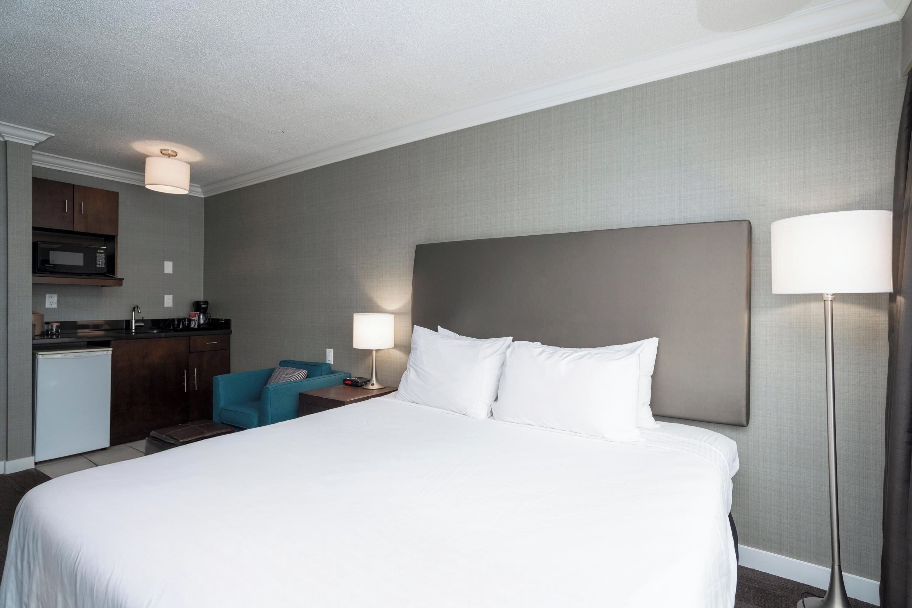 A hotel room with a bed, a desk, a chair, a microwave, and a lamp.