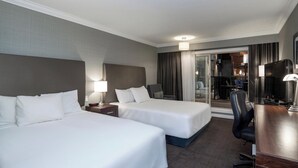 A hotel room with two beds, a desk, a chair, and a TV.