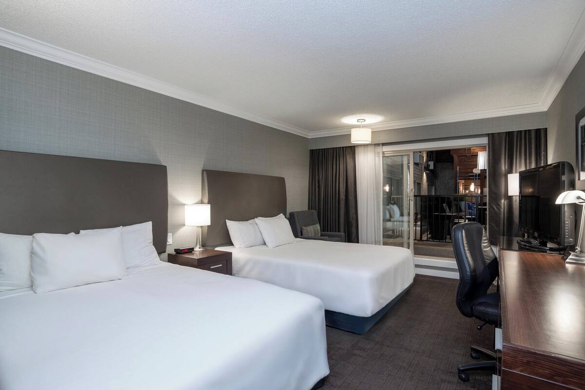 A hotel room with two beds, a desk, a chair, and a TV.