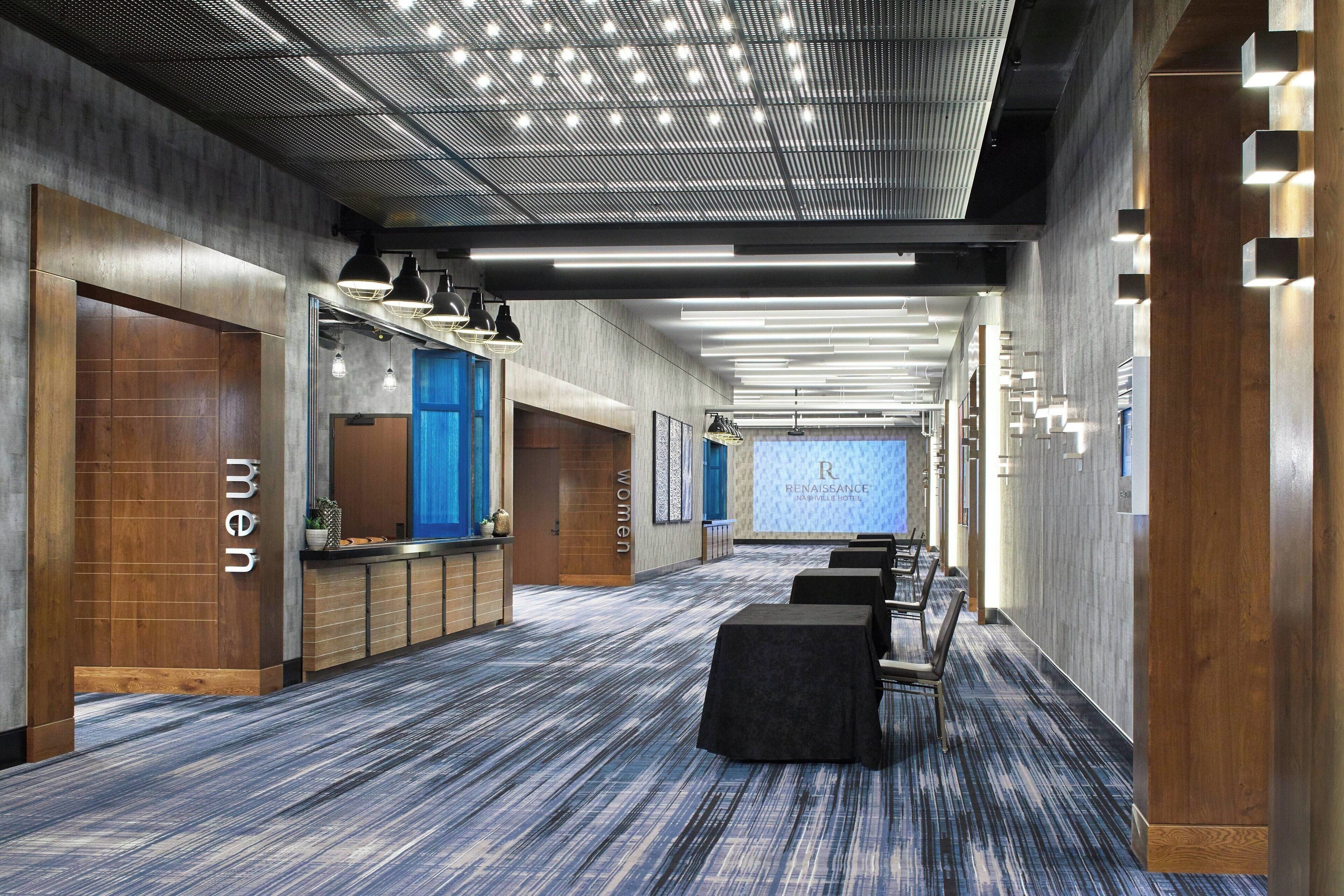 A modern hotel lobby with a long reception desk, a blue wall, and a projection screen displaying "Renaissance Hotel."