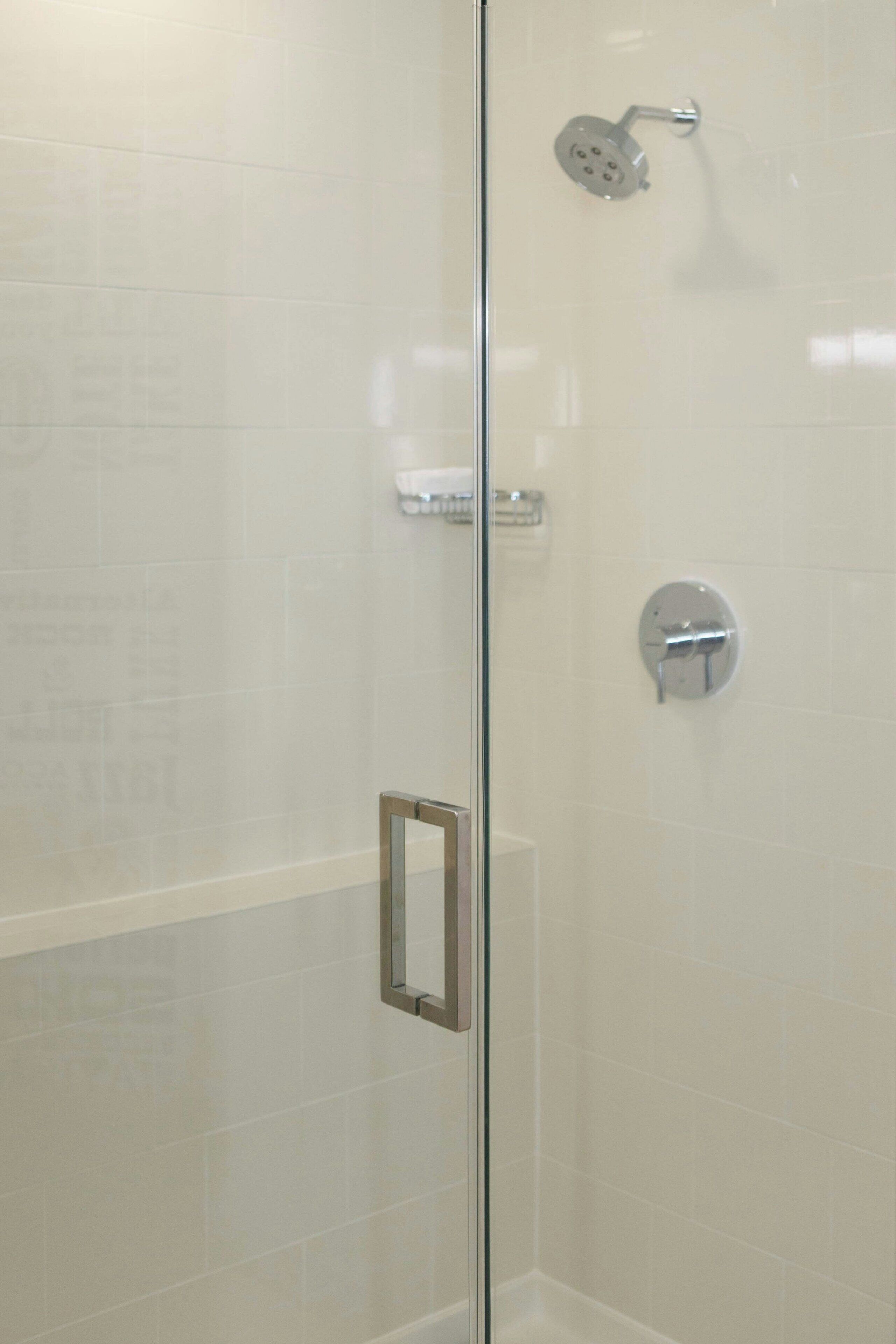 Ducha con cerramiento de vidrio, cabezal de ducha manual y llave de control en la pared.