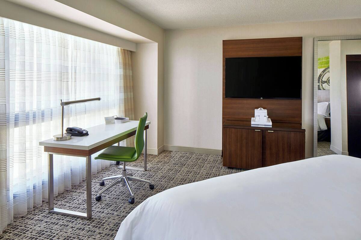Una habitación de hotel con cama, escritorio con silla, televisor y armario.