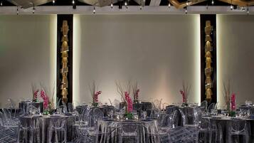 A banquet hall with round tables, clear chairs, and modern lighting fixtures.