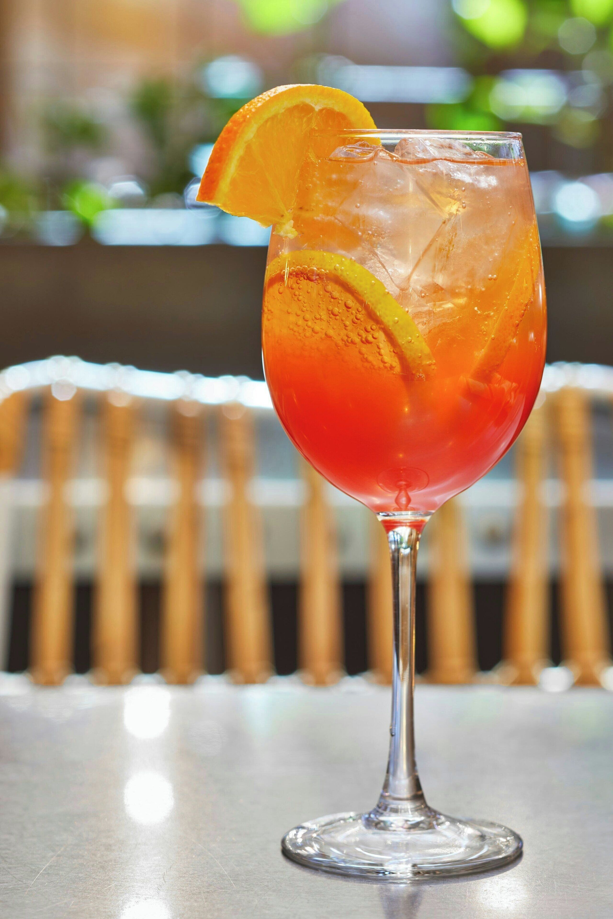 A cocktail glass with a slice of orange on the rim, filled with ice cubes.