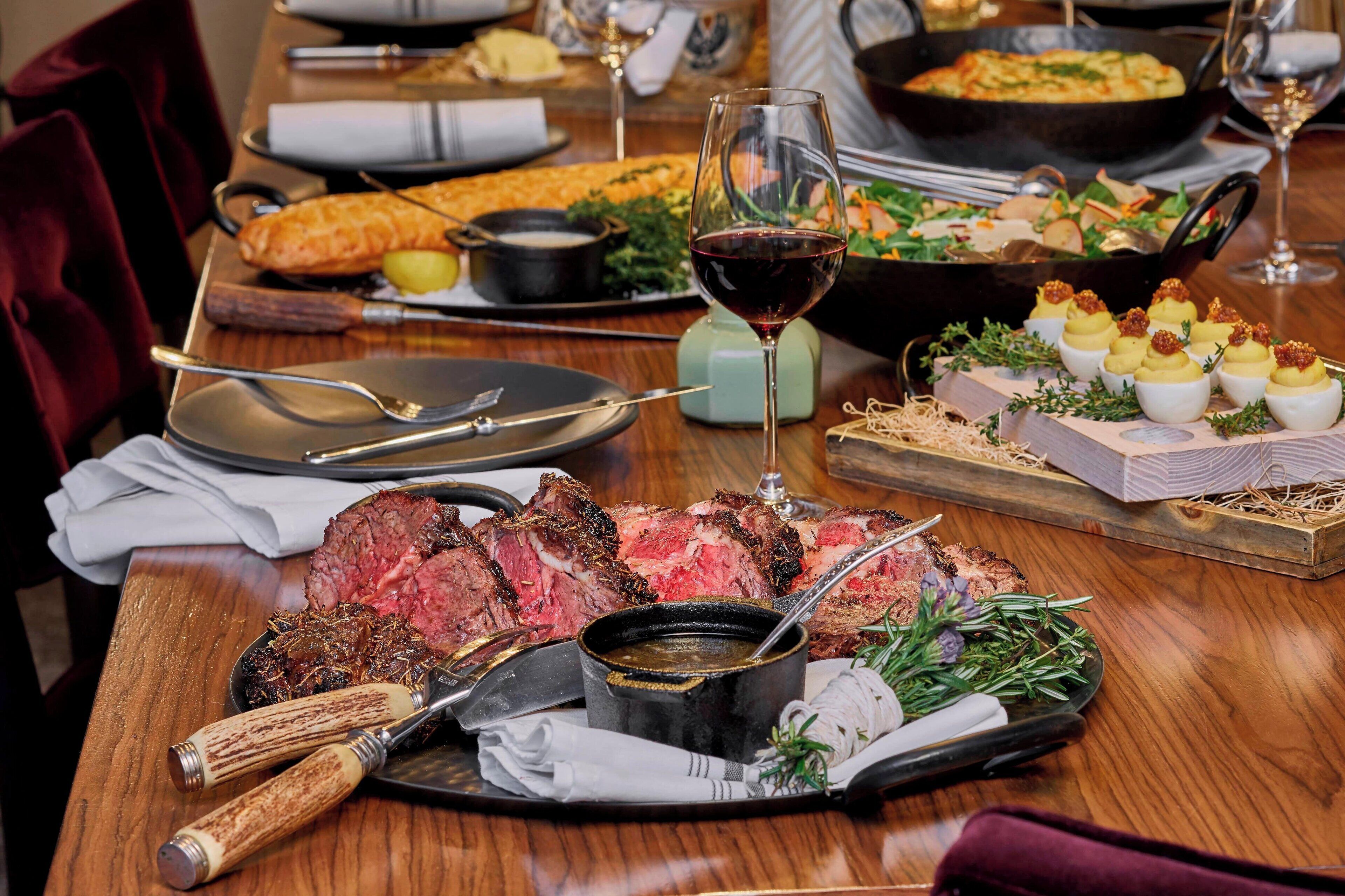 Una mesa de comedor con una variedad de platos, incluyendo carne, verduras y aperitivos.